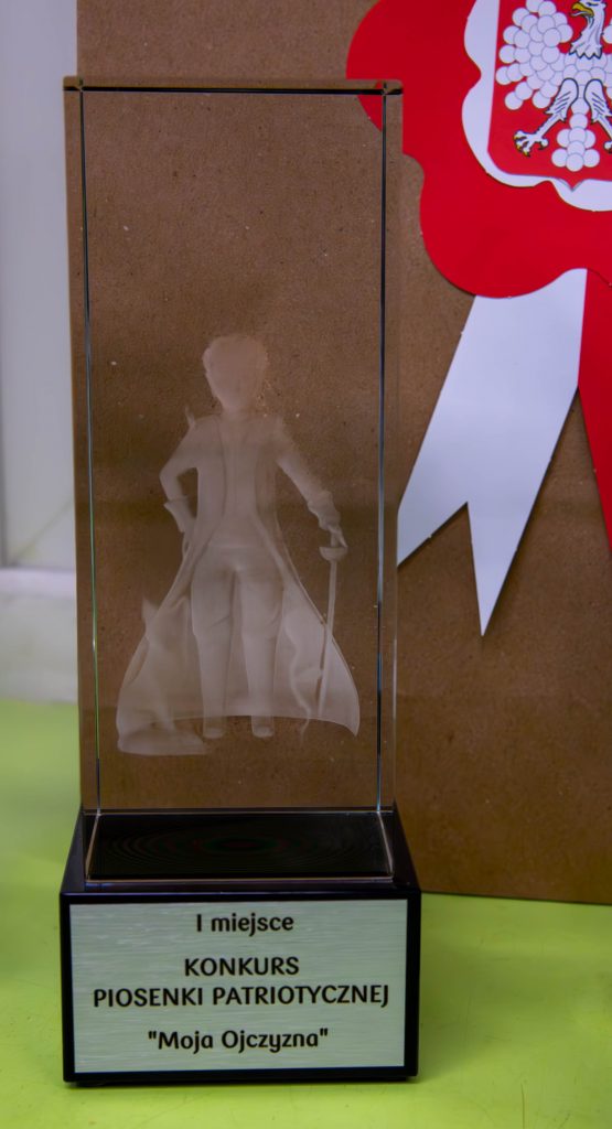 Na zdjęciu statuetka za I miejsce przedstawiająca "Małego Księcia" . W tle torba papierowa z biało-czerwonym kotylionem