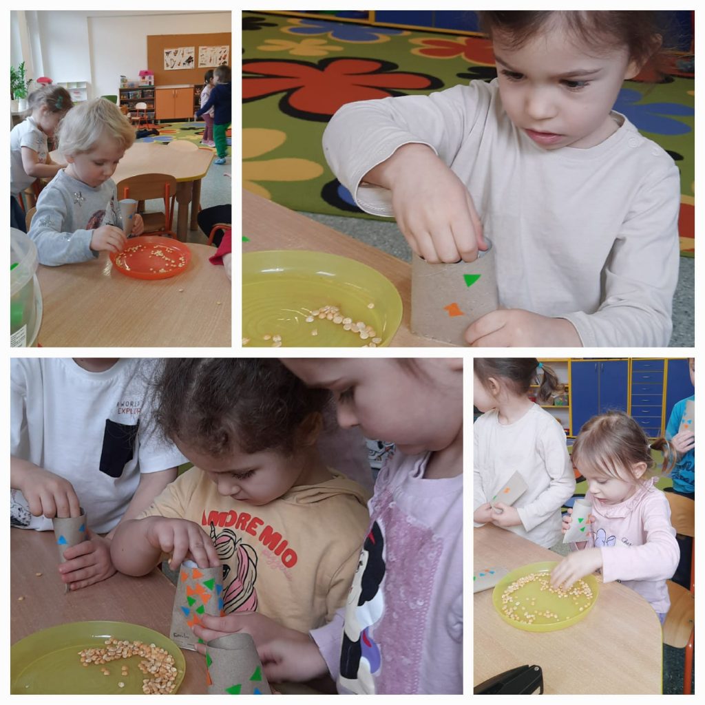 Zabawy sensoryczne. Na czterech zdjęciach dzieci wkładają ziarna grochu do rolki po papierze. W tle zdjęć sala przedszkolna, kolorowy dywan, jasne stoliki.