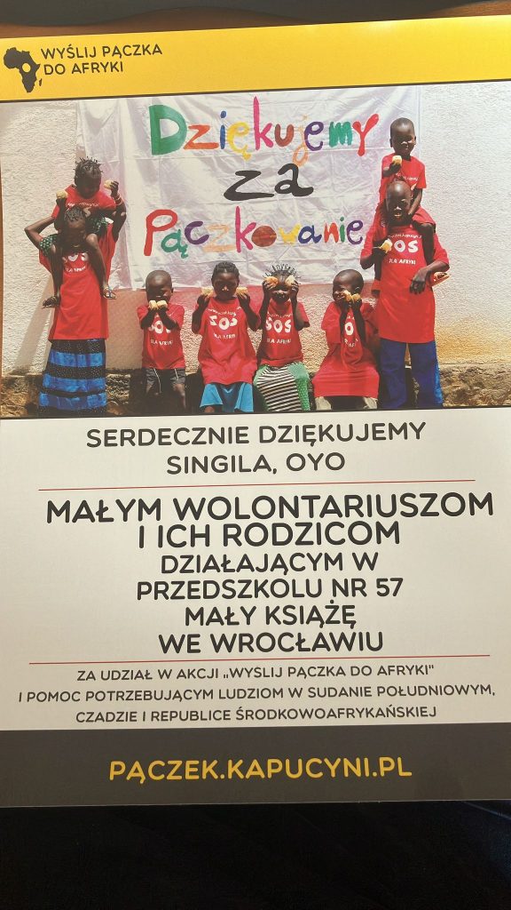 Grupa dzieci z Afryki w czerwonych koszulkach z białym napisem: "SOS DLA AFRYKI" oraz adresem strony internetowej akcji. Dwoje nastolatków - dziewczyna po lewej i chłopak z prawej strony - stoją po bokach, z młodszymi dziećmi "na barana", pośrodku czworo młodszych dzieci, trzymających pączki. Za nimi jasna ściana z zawieszonym na białym materiale kolorowy napisem: "Dziękujemy za Pączkowanie". U dołu podziękowanie dla małych wolontariuszy i ich rodziców Przedszkola Nr 57 Mały Książę we Wrocławiu, za udział w akcji "Wyślij pączka do Afryki" i pomoc potrzebującym ludziom w Sudanie Południowym, Czadzie , i Republice Środkowoafrykańskiej. U dołu napis" PĄCZEK.KAPUCYNI.PL