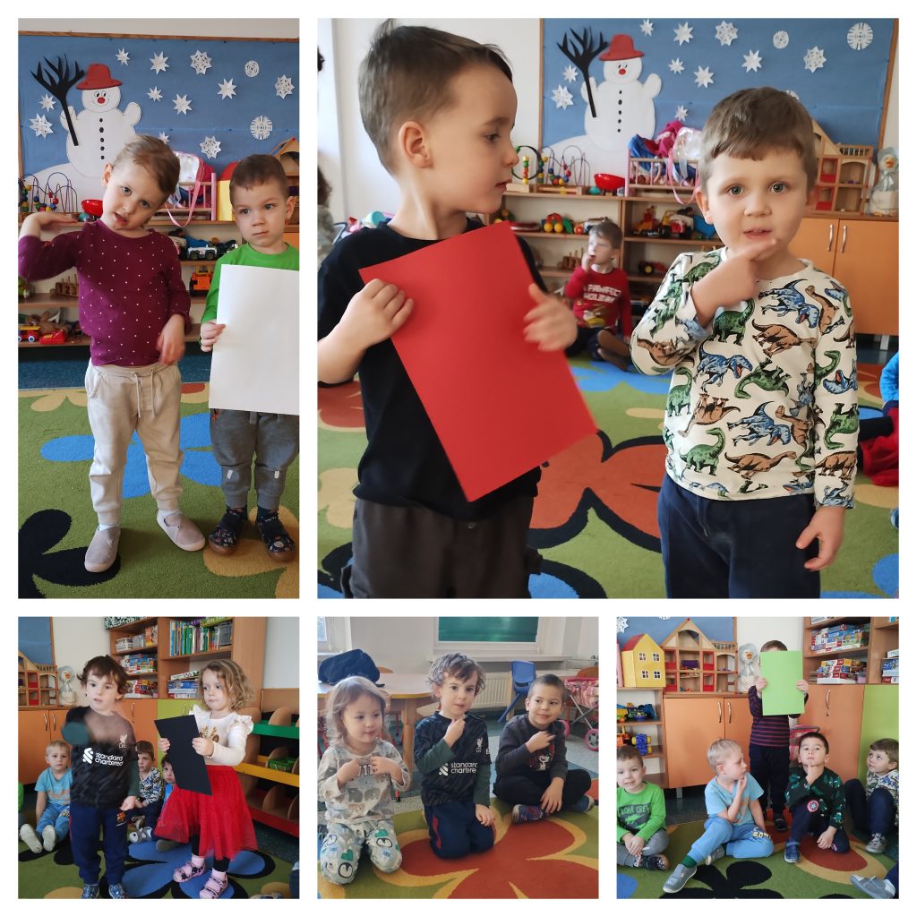 Obraz tworzy pięć zdjęć. Na pierwszym od góry dziewczynka i chłopiec. Chłopiec trzyma kartkę w kolorze białym, dziewczynka prezentuje nazwę koloru kartki w Polskim Języku Migowym. Na drugim zdjęciu dwóch chłopców. Chłopie po lewej stronie trzyma czerwoną kartkę, chłopiec po prawej pokazuje znak migowy dla koloru czerwonego. Na zdjęciu u dołu chłopiec pokazuje znak migowy oznaczając kolor czarny, a dziewczynka obok trzyma czarną kartkę papieru. Na kolejnym zdjęciu trzech chłopców siedzących na dywanie poznaje gest oznaczający w Polskim Języku Migowym Świętego Mikołaja. N ostatnim zdjęciu czworo dzieci na dywanie, również uczy się gestu na pokazanie Świętego Mikołaja.